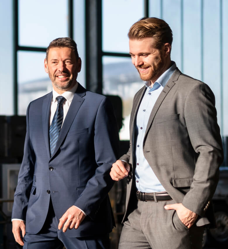 Two men in a suit standing next to each other and smiling. 