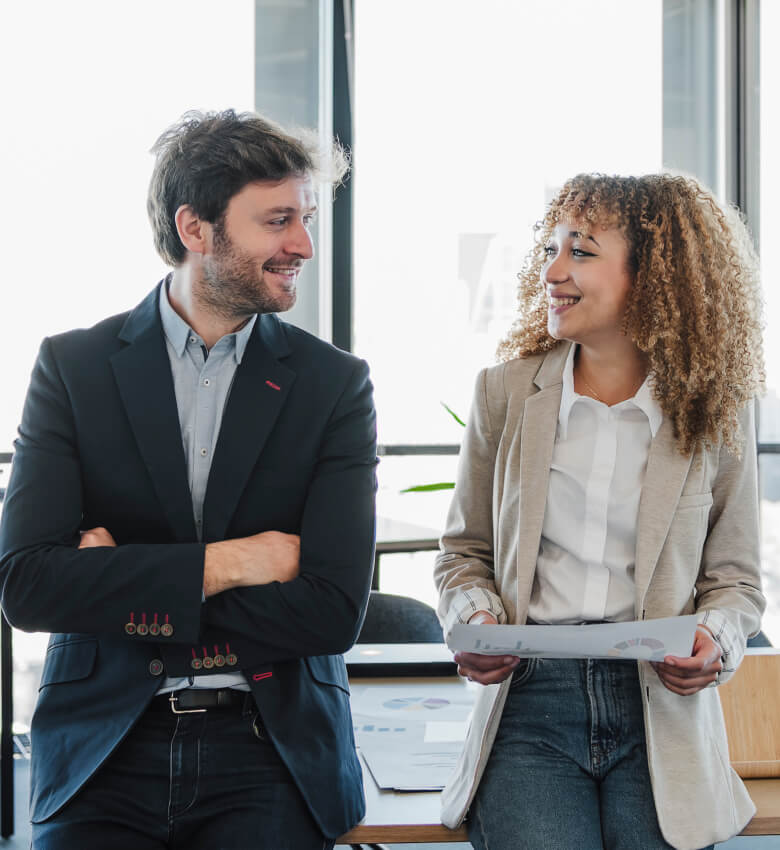 Two people standing next to each other in an office and smiling. 