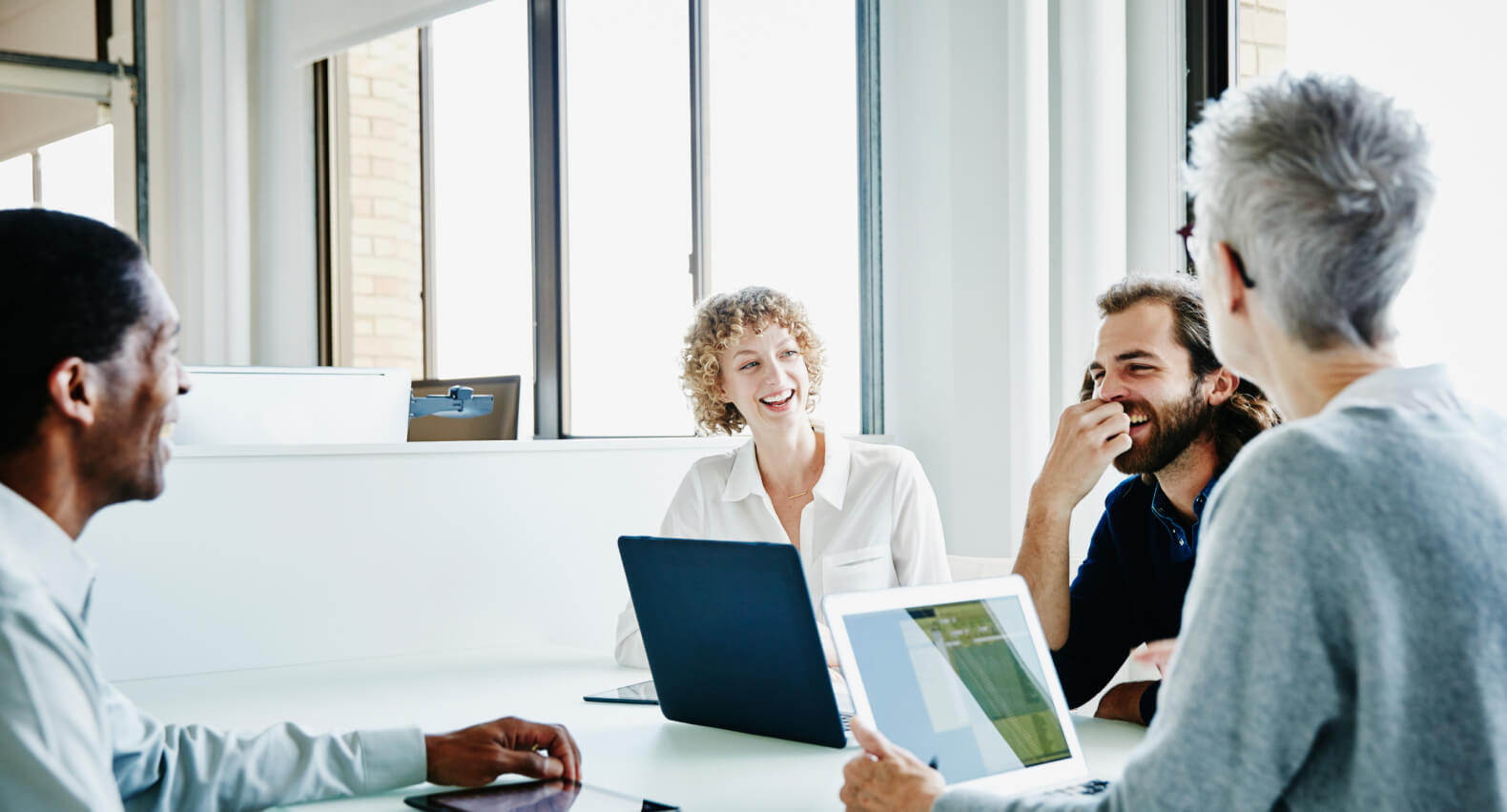 Four people sitting at a table laughing and on their laptops