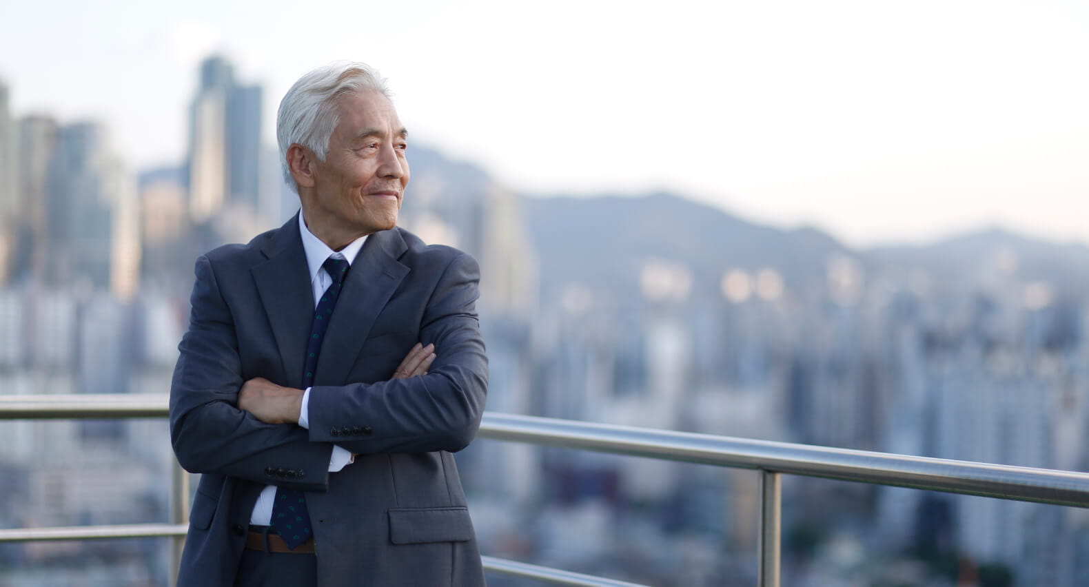 A man in a suit on a rooftop looking into the city. 